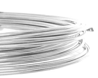 May include: Close-up of a coil of shiny, silver-colored wire. The wire is tightly wound, creating a circular shape. The bright metal reflects light, highlighting the smooth texture of the wire. The background is plain white.