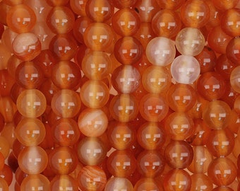 May include: Close-up of a collection of orange carnelian gemstone beads. The beads are round, polished, and have a translucent quality, with variations in color and pattern. The beads are strung together, creating a textured surface.