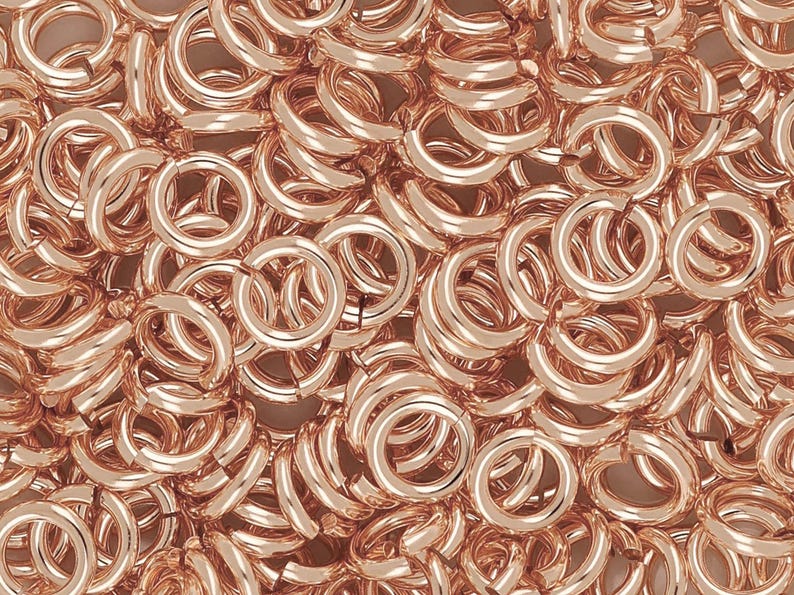 Puede incluir: Una imagen de primer plano de una gran pila de anillos de salto de oro rosa. Los anillos de salto son todos del mismo tama&ntilde;o y est&aacute;n dispuestos en un patr&oacute;n aleatorio.