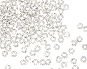 Puede incluir: Una gran cantidad de anillos de salto plateados, esparcidos sobre un fondo blanco. Los anillos de salto son pequeños y circulares, con un espacio en el anillo.