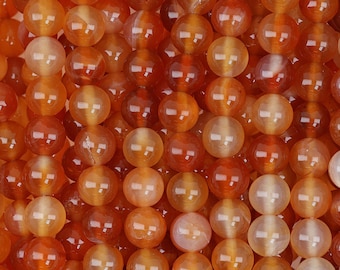 May include: A close-up of a strand of carnelian beads. The beads are a deep orange color and have a smooth, polished finish.