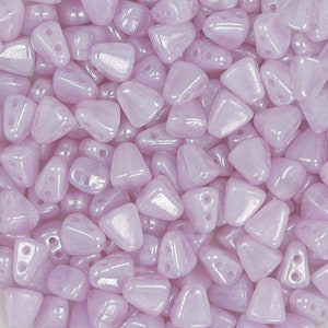 May include: A close-up of a pile of small, iridescent lavender triangle beads. The beads have two holes each and are made of glass.