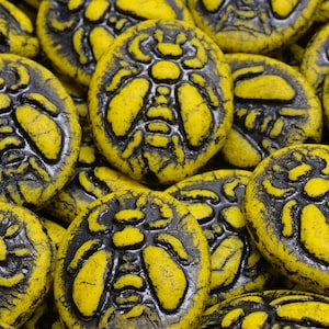 May include: A collection of yellow and black ceramic beads with a bee design. The beads are round and have a textured surface.