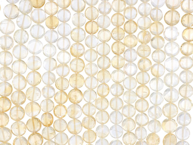 May include: Close-up of a collection of faceted, round beads in shades of yellow and clear. The beads are strung together, creating a pattern of light and color. The beads are likely gemstones, perfect for jewelry making.