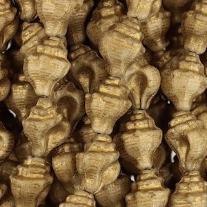 May include: A close-up of a pile of gold-colored seashell beads. The beads are small and have a detailed, textured surface.
