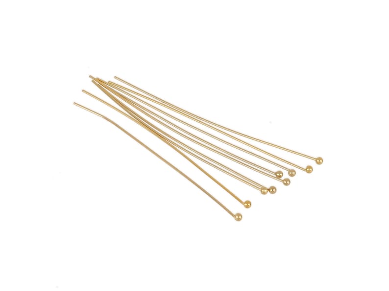 May include: A set of ten gold head pins with round heads. The pins are arranged in a fan shape.