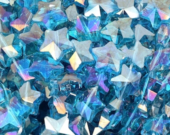 May include: A close-up of a pile of iridescent blue star-shaped glass beads. The beads are faceted and have a shimmery finish.