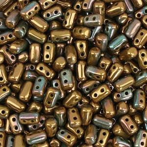 May include: A close-up image of a pile of small, gold-colored glass beads with a green iridescent sheen. The beads are rectangular in shape with two holes on each side.