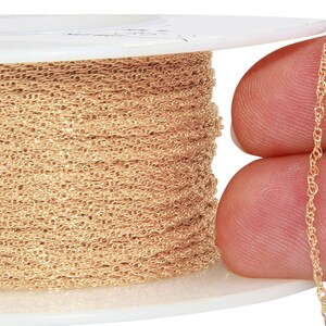 May include: A spool of gold-colored chain, with a close-up of the chain itself. The chain is delicate and has a slightly twisted design.