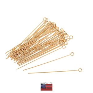 May include: A collection of gold-colored eye pins, ideal for jewelry making. The pins have a loop at one end and a straight wire extending from the loop. The image includes a small American flag in the bottom right corner.