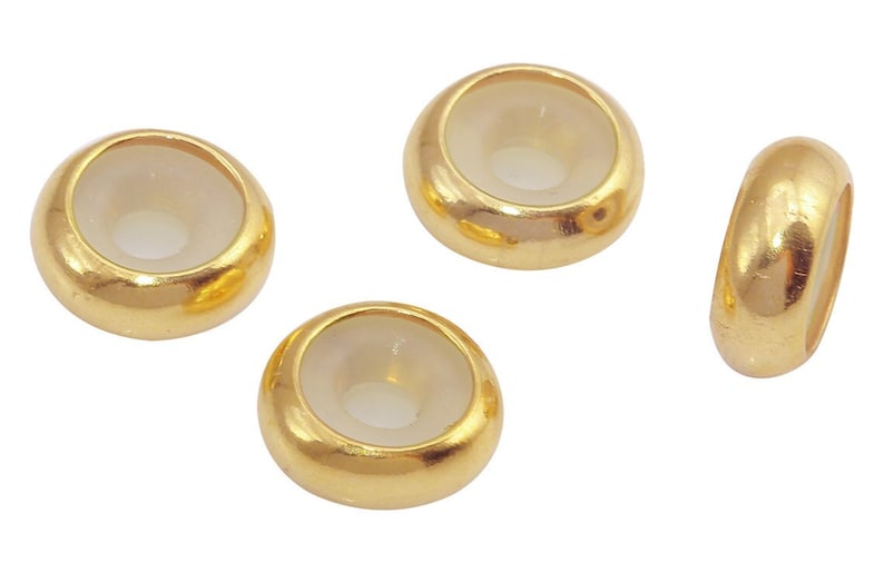 May include: Four gold-colored metal beads with a clear glass center. The beads are round and have a smooth surface.