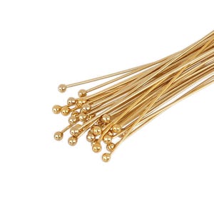 May include: A bunch of gold-colored head pins with round heads. The pins are arranged in a fan shape.