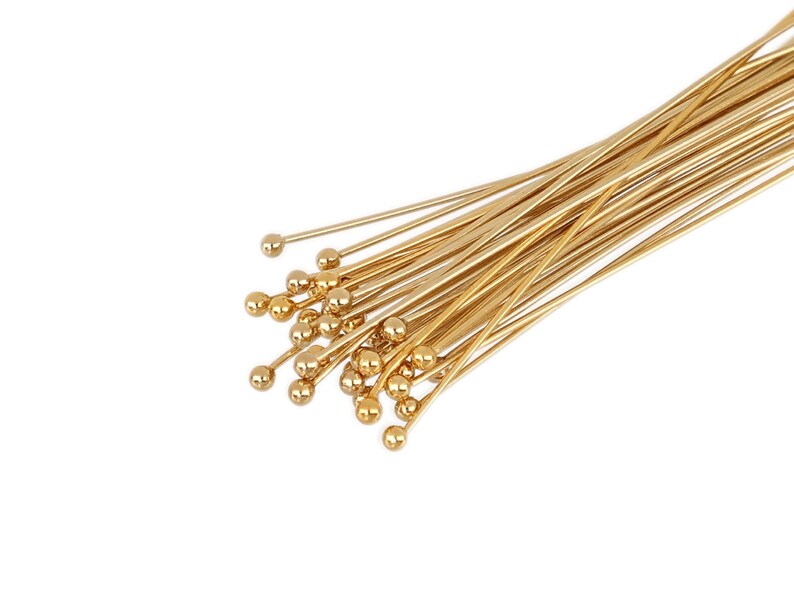 May include: A bunch of gold-colored head pins with round heads. The pins are arranged in a fan shape.