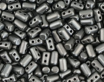 May include: A close-up view of a pile of small, silver-colored, two-hole beads. The beads are cylindrical in shape and have a matte finish.