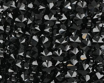 Puede incluir: Primer plano de una colección de pedrería negra con forma de flor. Cada pedrería tiene múltiples facetas que reflejan la luz, creando un efecto brillante. La pedrería está densamente empaquetada, llenando el marco.