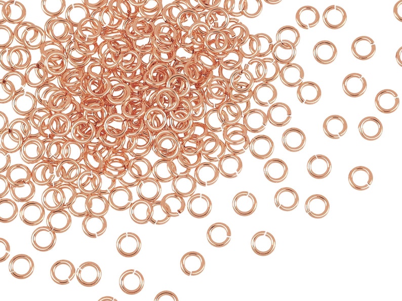 Puede incluir: Un mont&oacute;n grande de anillos de salto de oro rosa, con algunos dispersos alrededor del mont&oacute;n. Los anillos de salto son peque&ntilde;os y redondos, con un acabado liso.