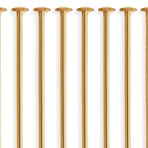 Puede incluir: Diez alfileres de metal de color dorado con cabezas redondas. Los alfileres est&aacute;n dispuestos en una fila.