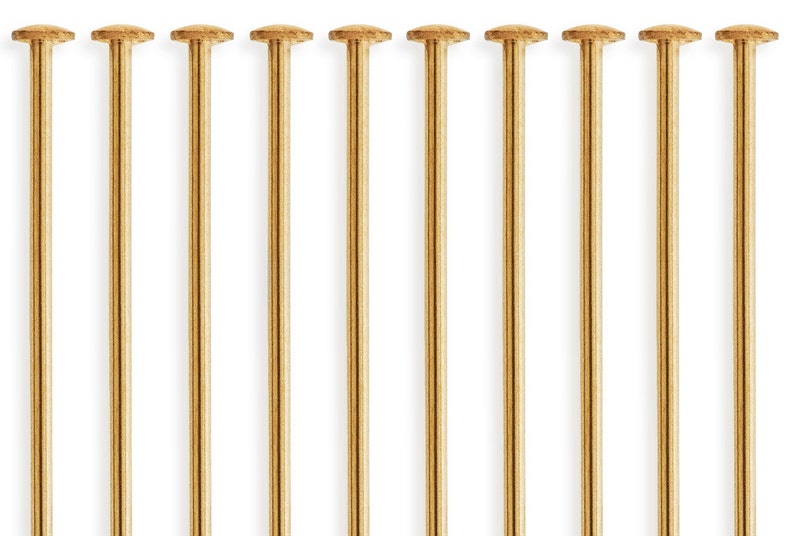 Puede incluir: Diez alfileres de metal de color dorado con cabezas redondas. Los alfileres est&aacute;n dispuestos en una fila.