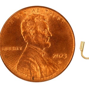 Op de afbeelding: Een gouden metalen krimpkraal, ongeveer ter grootte van een Nederlandse cent. De kraal is gevormd als een hoefijzer met afgeronde uiteinden.