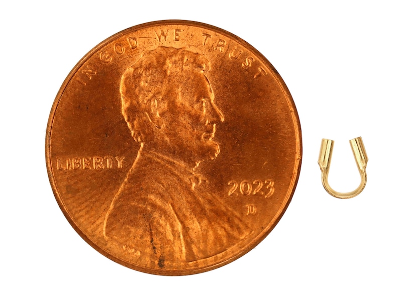 Op de afbeelding: Een gouden metalen krimpkraal, ongeveer ter grootte van een Nederlandse cent. De kraal is gevormd als een hoefijzer met afgeronde uiteinden.