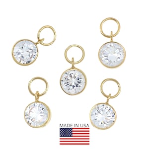 May include: Five gold-colored bezel-set charms with large, clear, round cubic zirconia stones. Each charm has a small loop at the top for attaching to a chain or bracelet. The words "MADE IN USA" are displayed with the American flag.