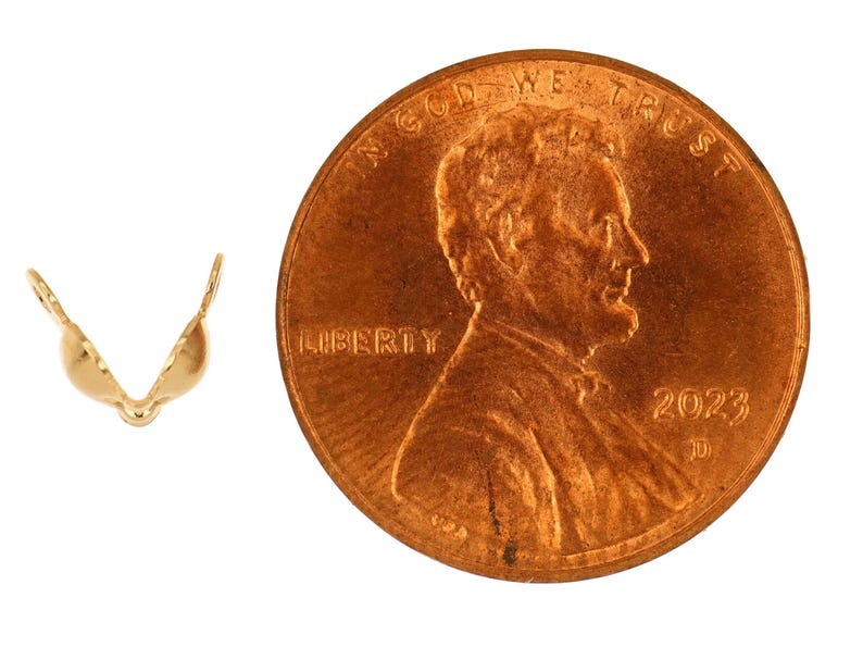 May include: A gold-colored jewelry finding, shaped like a small bra, next to a U.S. penny. The penny shows the profile of Abraham Lincoln and the year 2023. The jewelry finding is likely used in jewelry making.
