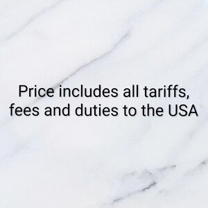 May include: A white marble background with grey veining featuring the black text: Price includes all tariffs, fees and duties to the USA. The text is centered and clearly legible against the smooth, polished stone surface.