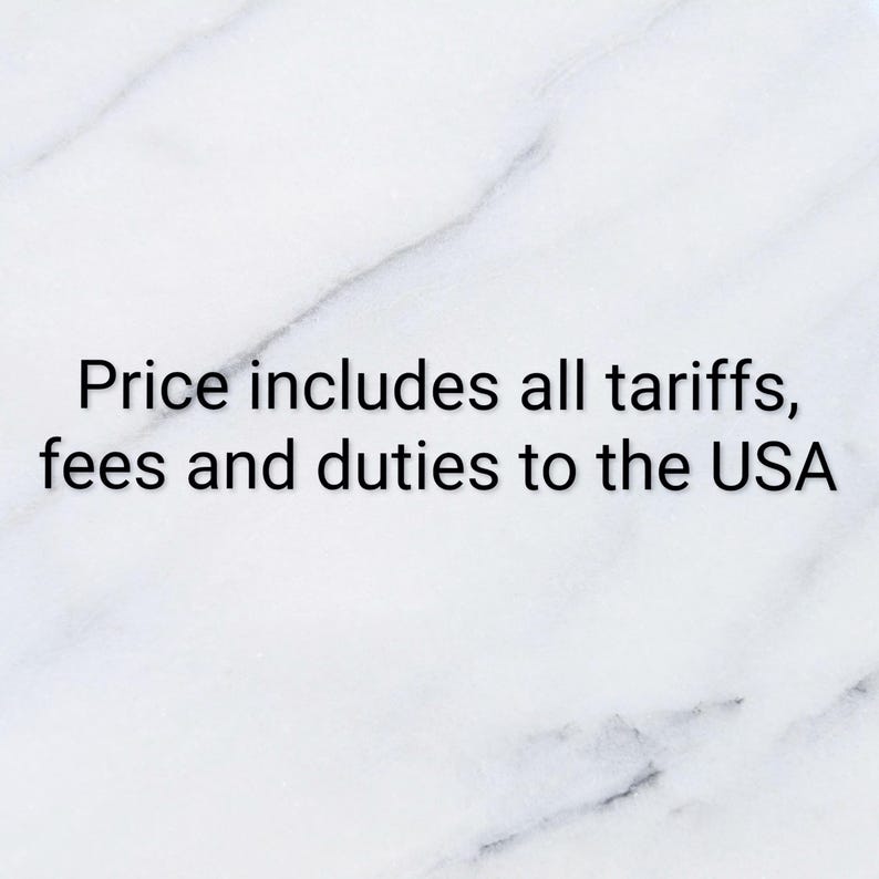 May include: A white marble background with grey veining featuring the black text: Price includes all tariffs, fees and duties to the USA. The text is centered and clearly legible against the smooth, polished stone surface.