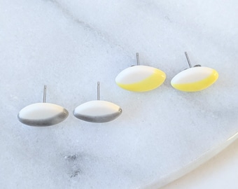 May include: Two pairs of stud earrings with a smooth, oval-shaped design. One pair features a white and yellow color-blocked finish, while the other pair displays a white and grey color-blocked finish. Each earring has a silver-toned metal post.