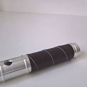 May include: A silver metal tube with a brown leather wrap. The tube has a small hole in the side.