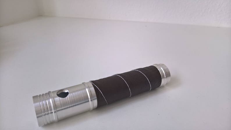 May include: A silver metal tube with a brown leather wrap. The tube has a small hole in the side.