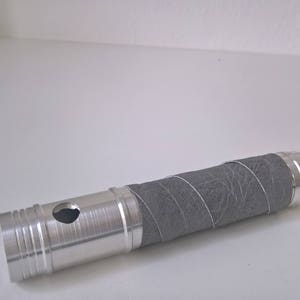 May include: A silver metal tube with a grey fabric covering. The tube has a small hole in the side.