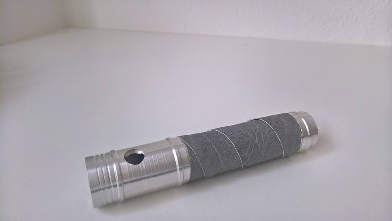 May include: A silver metal tube with a grey fabric covering. The tube has a small hole in the side.