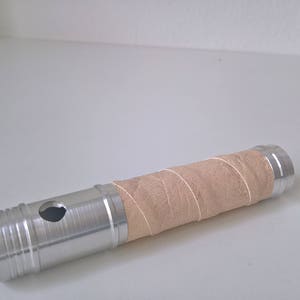 May include: A silver metal tube with a brown paper wrap. The tube has a hole in the side and a textured surface.