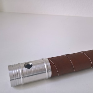 May include: A silver metal tube with a brown leather wrap. The tube has a hole in the side.