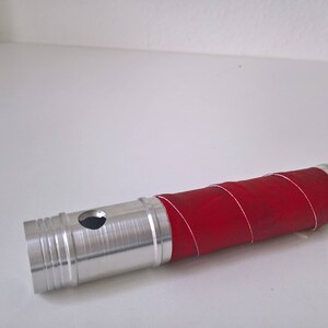 May include: A silver metal tube with a red rubber sleeve wrapped around it. The tube has a small hole in the side.