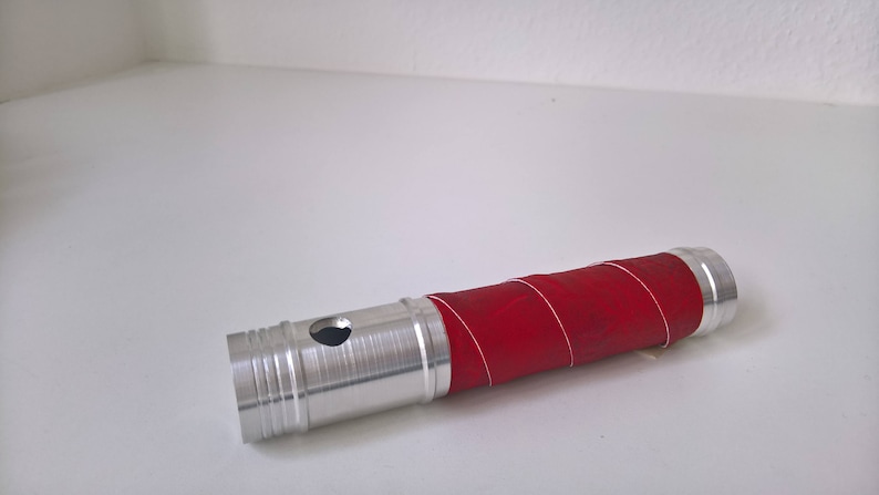 May include: A silver metal tube with a red rubber sleeve wrapped around it. The tube has a small hole in the side.