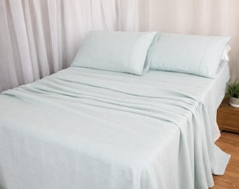 Puede incluir: Un juego de cama que incluye una sábana encimera y dos fundas de almohada a juego en color verde menta claro. La ropa de cama presenta un tejido con textura sutil y está colocada cuidadosamente sobre un colchón, creando un aspecto uniforme.