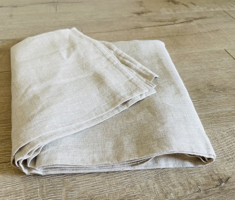 K&ouml;nnte beinhalten: Eine gefaltete Tischdecke aus Leinen in hellgrauer Farbe. Die Tischdecke ist aus nat&uuml;rlichem Leinenstoff gefertigt und hat eine weiche, strukturierte Oberfl&auml;che.