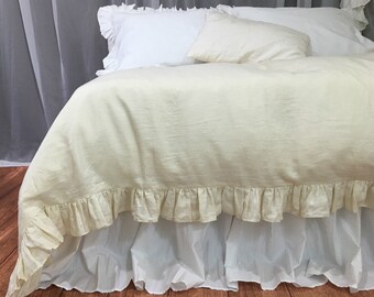 May include: A cream-colored linen duvet cover with a ruffled edge. The duvet is on a bed with a white ruffled bed skirt.