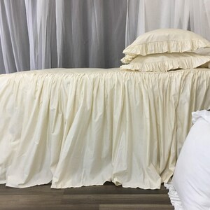 May include: A cream-colored bed skirt with a ruffled edge. The skirt is made of a soft, flowing fabric and is perfect for adding a touch of elegance to any bedroom.