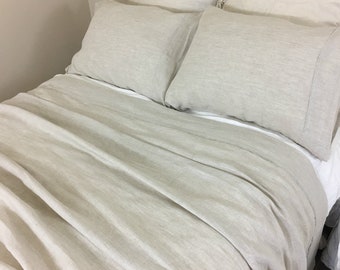 Puede incluir: Un primer plano de un juego de ropa de cama de lino en color beige claro. La ropa de cama está hecha de tela de lino natural y tiene un aspecto relajado y casual. El juego incluye una sábana plana, una sábana ajustable y dos fundas de almohada.
