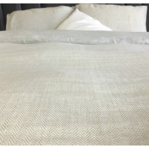 May include: A close-up of a white linen duvet cover with a herringbone pattern. The duvet cover is on a bed with white pillows.