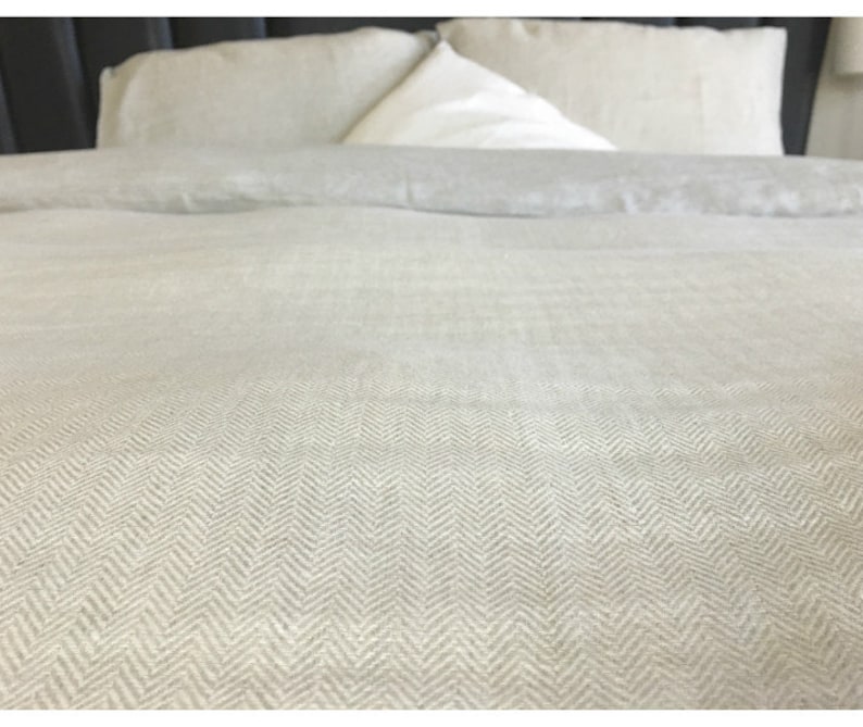 May include: A close-up of a white linen duvet cover with a herringbone pattern. The duvet cover is on a bed with white pillows.