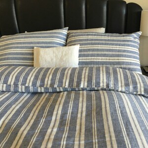 Pu&ograve; includere: Un copripiumino in lino a righe blu e bianche con due federe abbinate e un cuscino decorativo bianco. La biancheria da letto &egrave; su una testata in pelle nera.