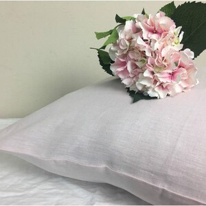 May include: A soft, light pink pillow with a white border. A bouquet of pink hydrangeas is resting on top of the pillow.