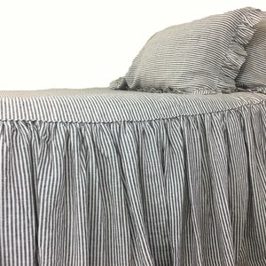 May include: A white and black striped bed skirt with a ruffled edge. The skirt is made of linen and has a simple, elegant design.