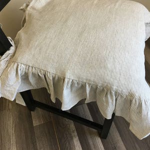 May include: A chair cushion with a ruffled edge. The cushion is made of a beige and white striped fabric. The cushion is tied to the chair with fabric ties. The chair is black.