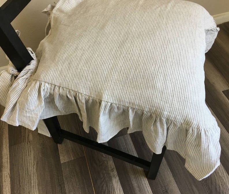 May include: A chair cushion with a ruffled edge. The cushion is made of a beige and white striped fabric. The cushion is tied to the chair with fabric ties. The chair is black.