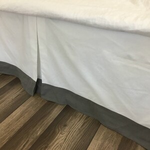 May include: White bed skirt with a gray trim. The skirt is pleated and has a simple design.